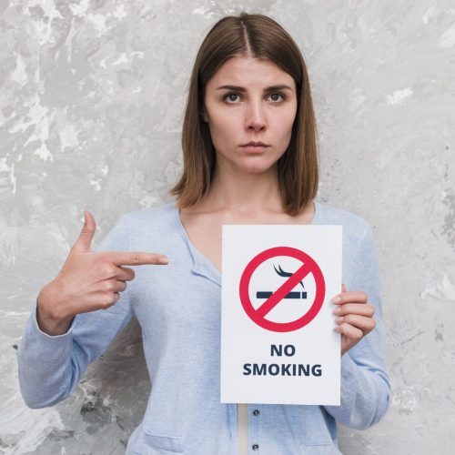 woman-pointing-finger-no-smoking-poster-standing-near-weathered-wall (1)